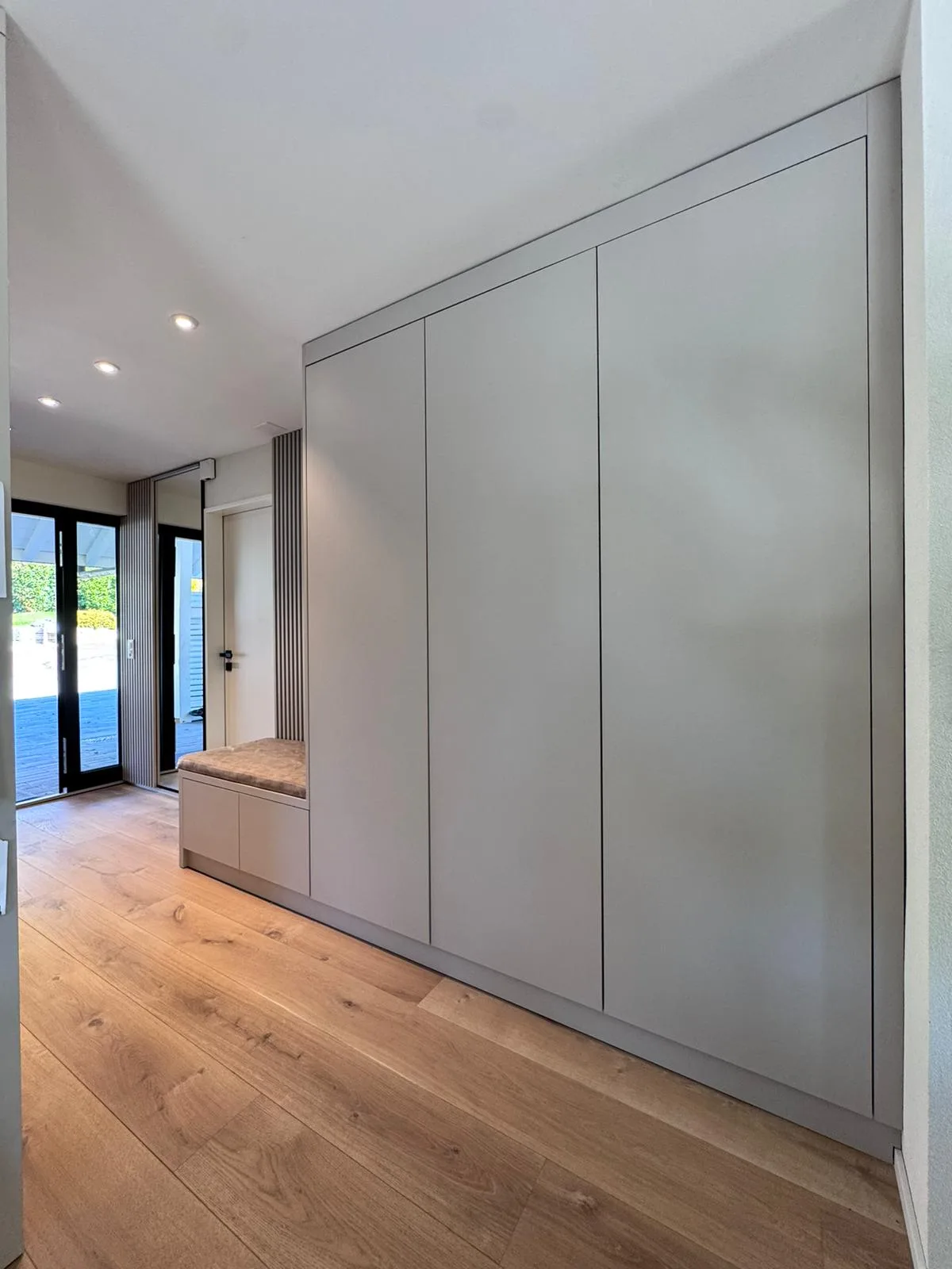 Heller Eingangsbereich mit deckenhohem Einbauschrank, Sitzbank und Holzboden in modernem Design