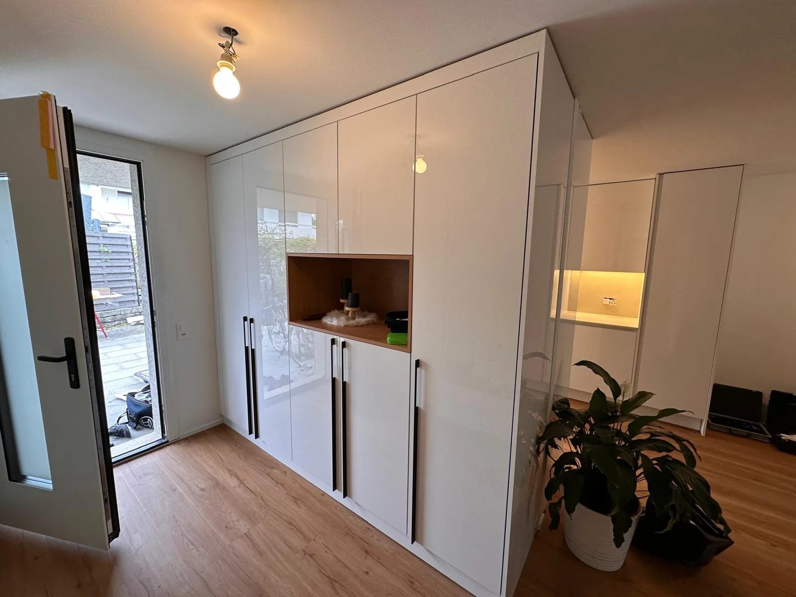 Eingangsbereich mit weißem Einbauschrank, offener Holz-Nische und integrierter Beleuchtung