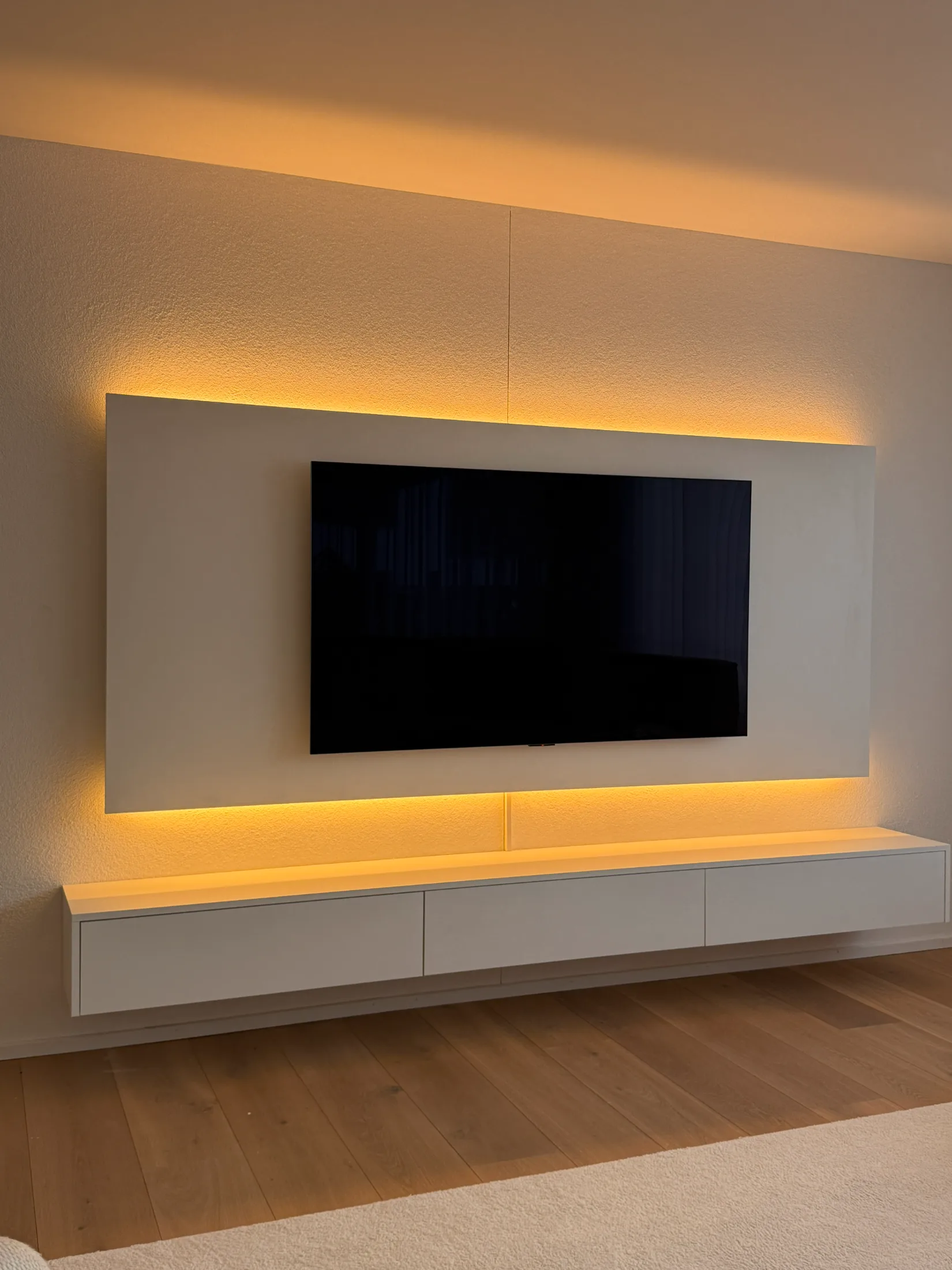 Moderne weiße TV-Kommode mit schwebender Bauweise und großem Wandpaneel mit warmer LED-Hintergrundbeleuchtung
